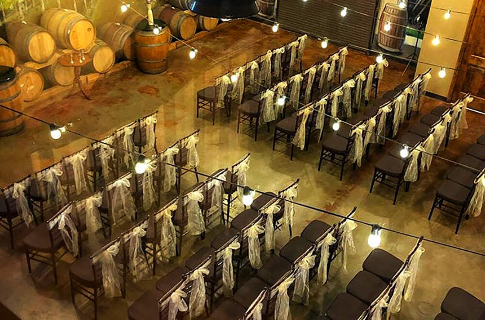 Strings of warm lights are draped above an indoor rustic wedding ceremony. 