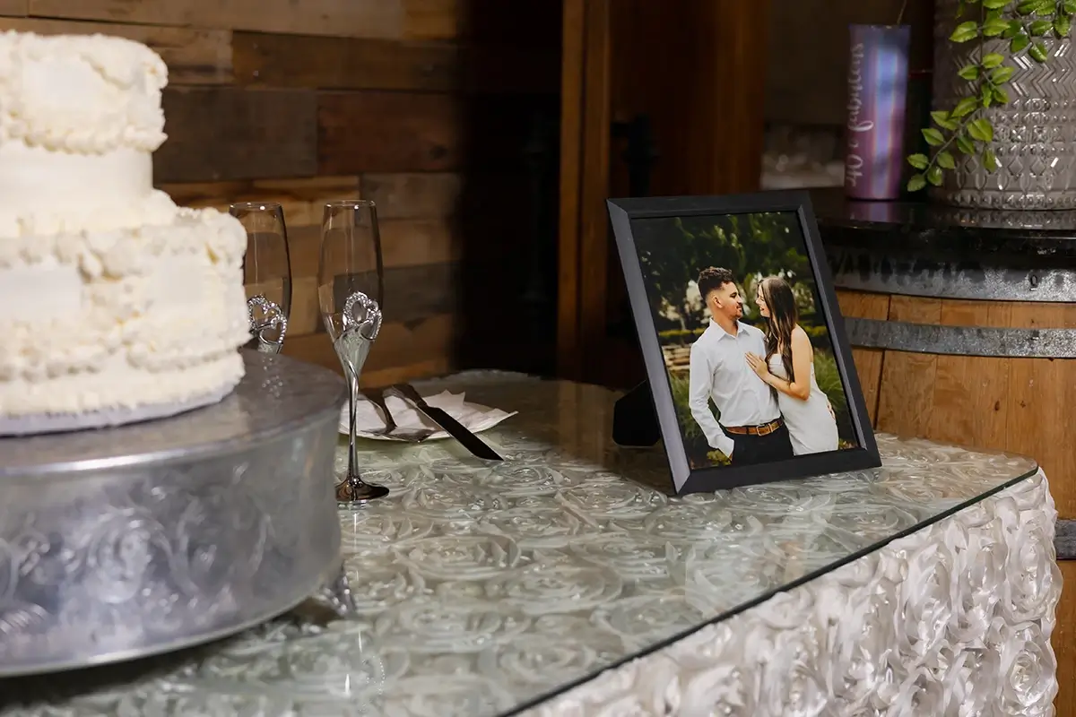Wedding cake and champagne flutes beside a framed couple&rsquo;s photo on a decorated reception table.